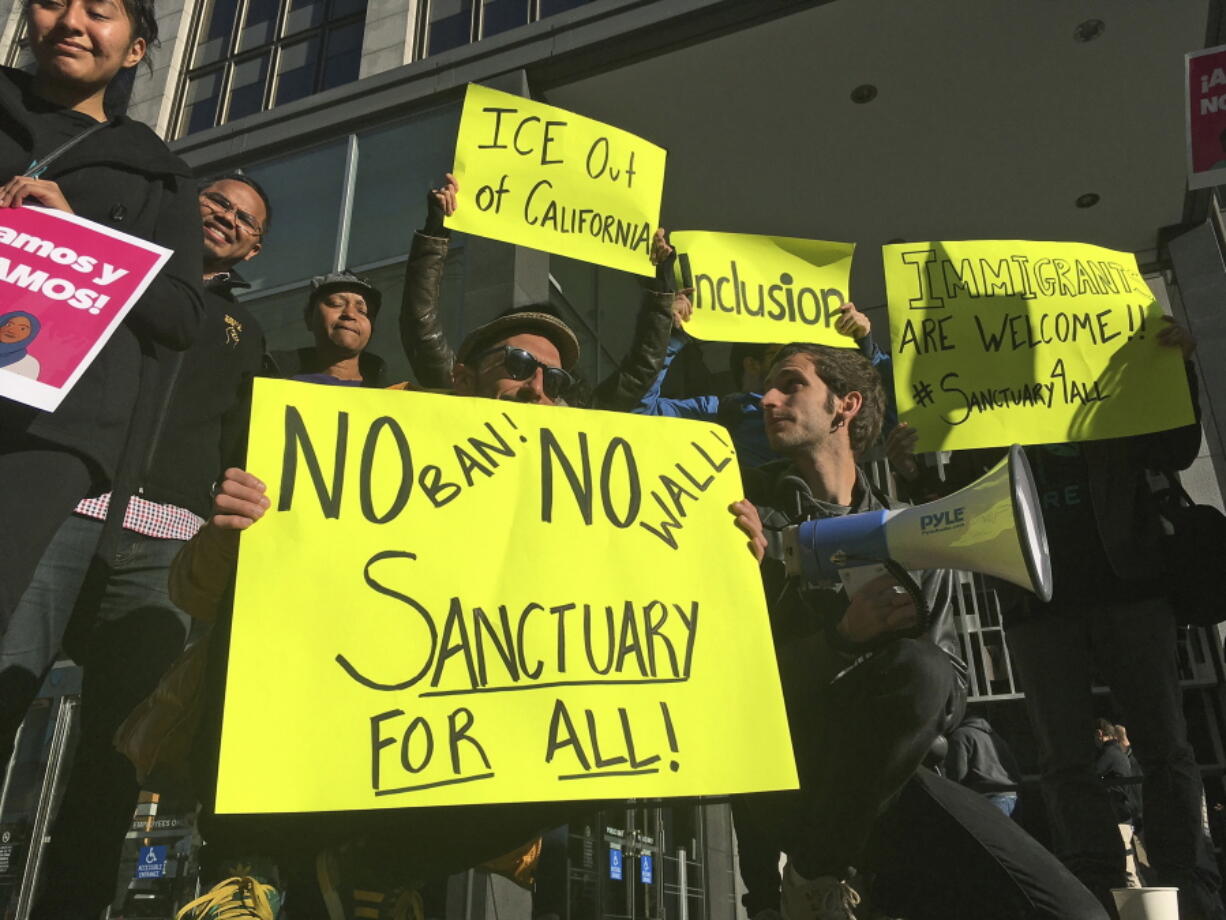 FILE - In this April 14, 2017, file photo, protesters hold up signs outside a courthouse in San Francisco. President Donald Trump’s executive order threatening to withhold funding from “sanctuary cities” that limit cooperation with immigration authorities is unconstitutional, but a judge went too far when he blocked its enforcement nationwide, a U.S. appeals court ruled Wednesday, Aug. 1.