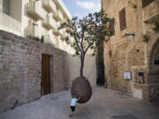 In this Saturday, July 28, 2018 photo, a child plays next to a 100-year-old orange tree hanging above the ground in the old city of Jaffa, Israel. Israel’s port city of Jaffa is an ancient place. Today glass towers and modern apartment complexes rise amid Jaffa’s old white stone buildings. It’s famous for its flea market and hummus cafes. But visitors will also find trendy bars, galleries and boutiques.