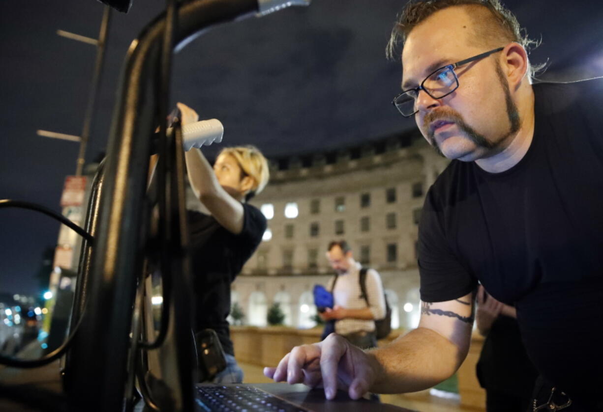 Robin Bell, right, works on his laptop to project a message in light on the Trump International Hotel on July 23 in Washington. In a city with a long tradition of leftist street activism, Bell has become something of a local celebrity. Every few weeks, Bell puts messages of protest on the side of the Trump International Hotel.