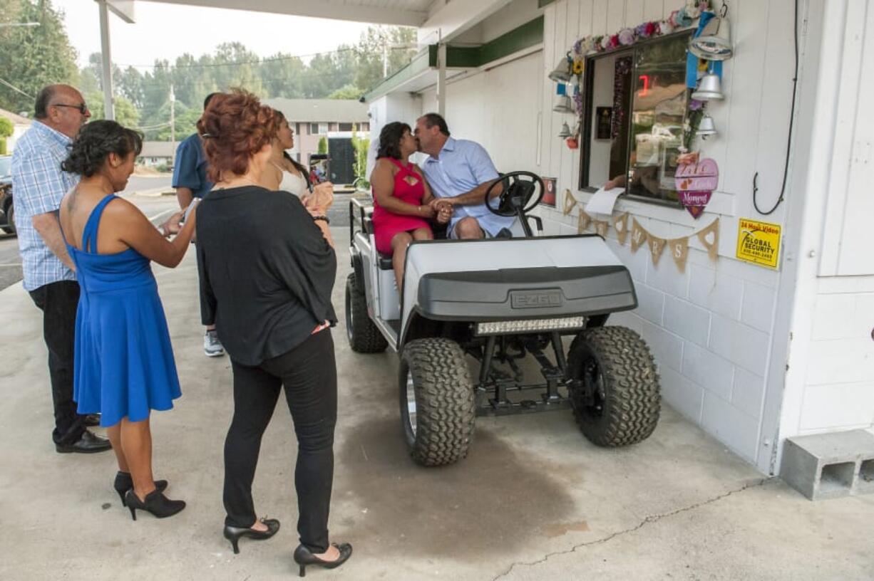 Family and friends watch as James Coen and Cristina Wardwell of Molalla, Ore., kiss to end their wedding ceremony at the drive-thru window of Mystic Gardens floral shop in Camas. Owner Leslie Rick started performing drive-thru weddings at her shop in January and has been marrying couples for more than 20 years.