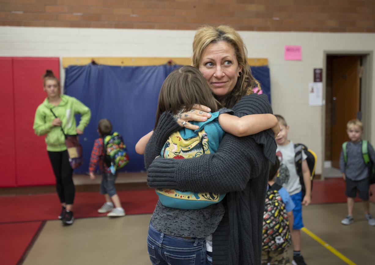 Mary Moore, facing, shares a hug with her daughter, Ruby Ketchum, 5, in the gym before joining her kindergarten class during the first day of school at Peter S. Ogden Elementary School on Wednesday morning. Students in Vancouver Public Schools returned to class after three days of striking last week.