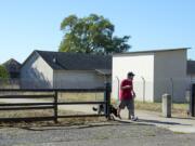 The stockade at Fort Vancouver National Site, left, is obscured by a historical warehouse building Thursday morning as Vancouver resident Greg Martin walks his 6-month-old dog, Sage.