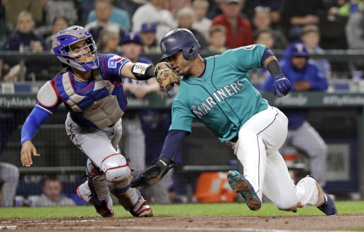 Seattle Mariners’ Jean Segura, right, avoids a tag by Texas Rangers catcher Robinson Chirinos while sliding safely home in the second inning of a baseball game Friday, Sept. 28, 2018, in Seattle.