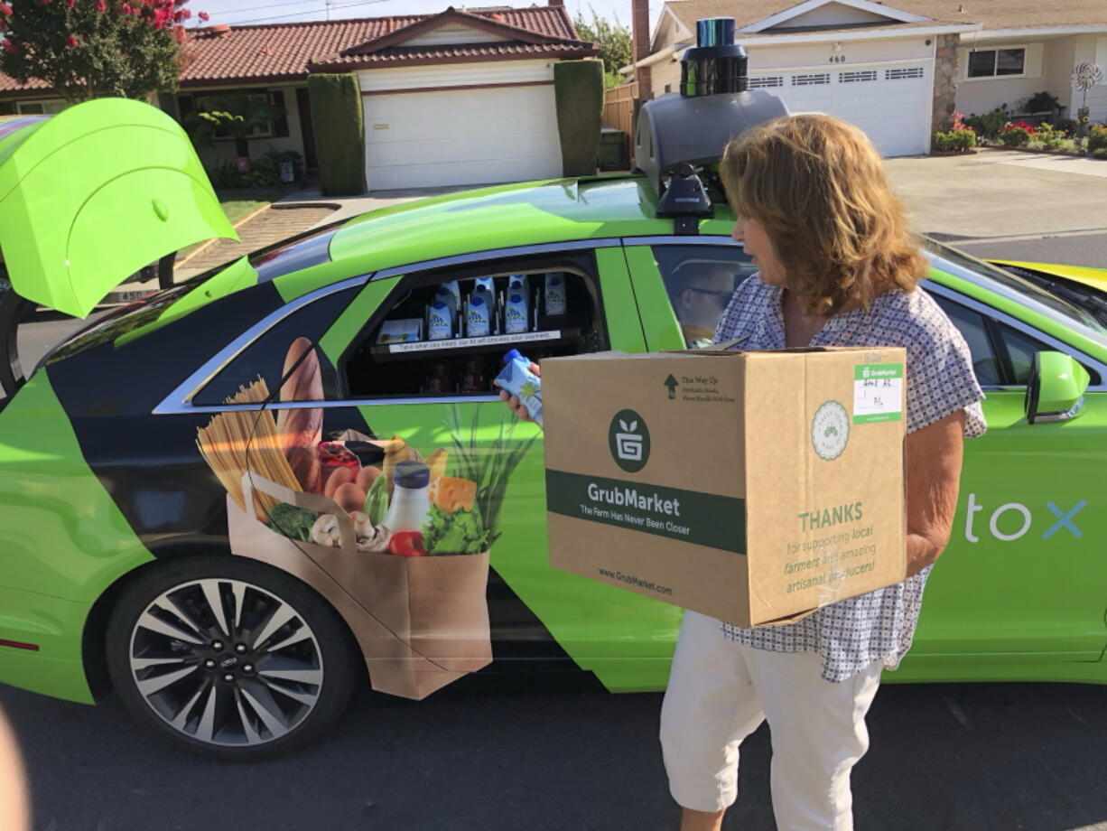 Customer Maureen Blaskovich grabs a coconut water from the backseat window of a self-driving car — a Lincoln MKZ outfitted with technology by AutoX — in San Jose, Calif.