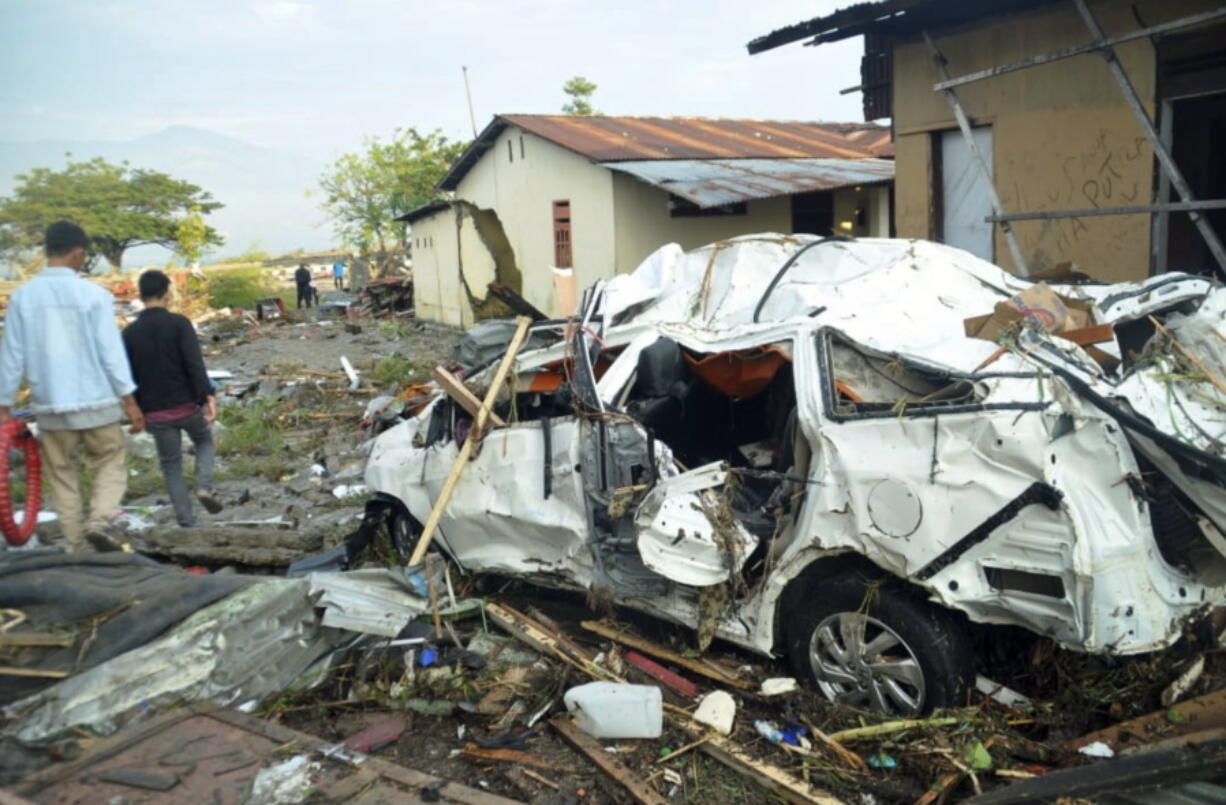 Indonesian men walk past the wreckage of a car following earthquakes and a tsunami in Palu, Central Sulawesi, Indonesia, Saturday, Sept. 29, 2018. A tsunami swept away buildings and killed large number of people on the Indonesian island of Sulawesi, dumping victims caught in its relentless path across a devastated landscape that rescuers were struggling to reach Saturday, hindered by damaged roads and broken communications.