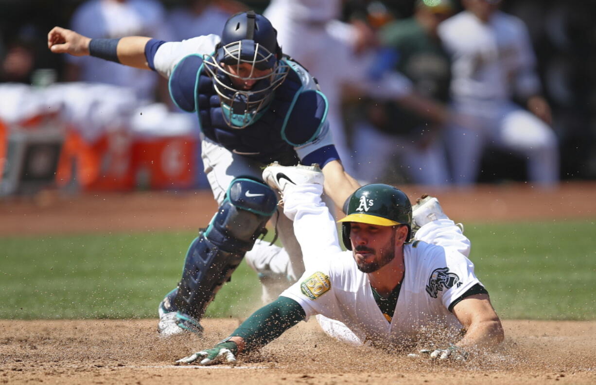 Oakland Athletics’ Matt Joyce slides to score beneath the tag of Seattle Mariners catcher Mike Zunino in the sixth inning of a baseball game Sunday, Sept. 2, 2018, in Oakland, Calif. Joyce scored on a single by A’s Marcus Semien.