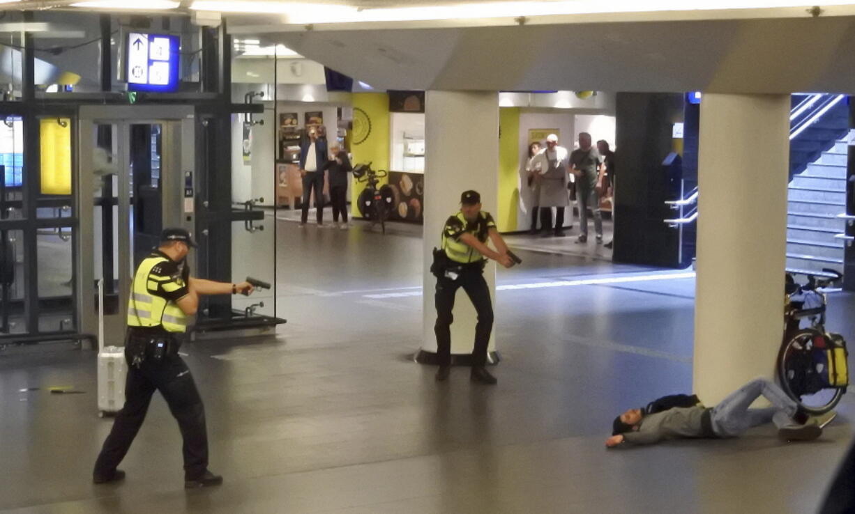 Dutch police officers point their guns at a wounded 19-year-old man who was shot by police after stabbing two people in the central railway station in Amsterdam, the Netherlands, Friday Aug. 31, 2018. Police investigators in Amsterdam included an extremist attack as a possible motive for the stabbings of two people at a busy railway station Friday as authorities in the Dutch capital reported that the suspect shot by police is an Afghan citizen.