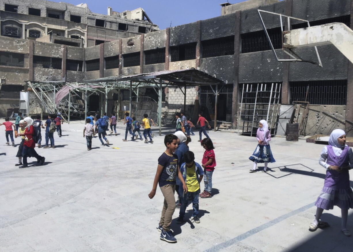 In this Wednesday, Sept 5, 2018 photo, Syrian students play in the courtyard of a school whose walls are still charred and pockmarked with bullets from recent fighting in the town of Douma, in the eastern Ghouta region, near the Syrian capital Damascus, Syria. Millions of Syrian children return to school as the country’s conflict simmers down. The Syrian government is keen to project a sense of normalcy, opening hundreds of newly renovated schools and calling on students to wear uniforms, which were shed in years of chaos. But humanitarians say the war is far from over, particularly its scars on children.