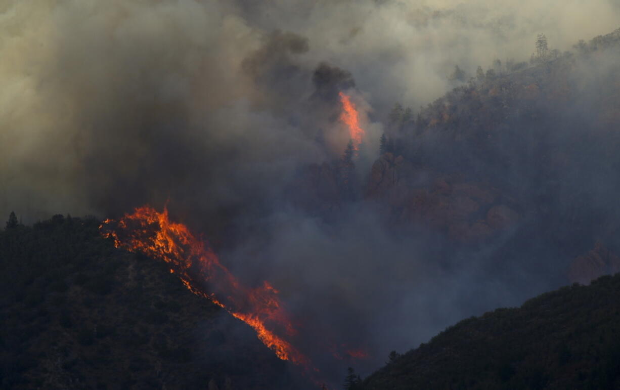 In this Wednesday, Sept. 12, 2018, photo hot spots flare up near a rock formation a wildfire burns in northern Juab County, Utah. A fast-moving Utah wildfire fanned by high-winds has more than doubled in size as it burns through dry terrain and forces evacuations of hundreds of homes, the U.S. Forest Service said Friday.