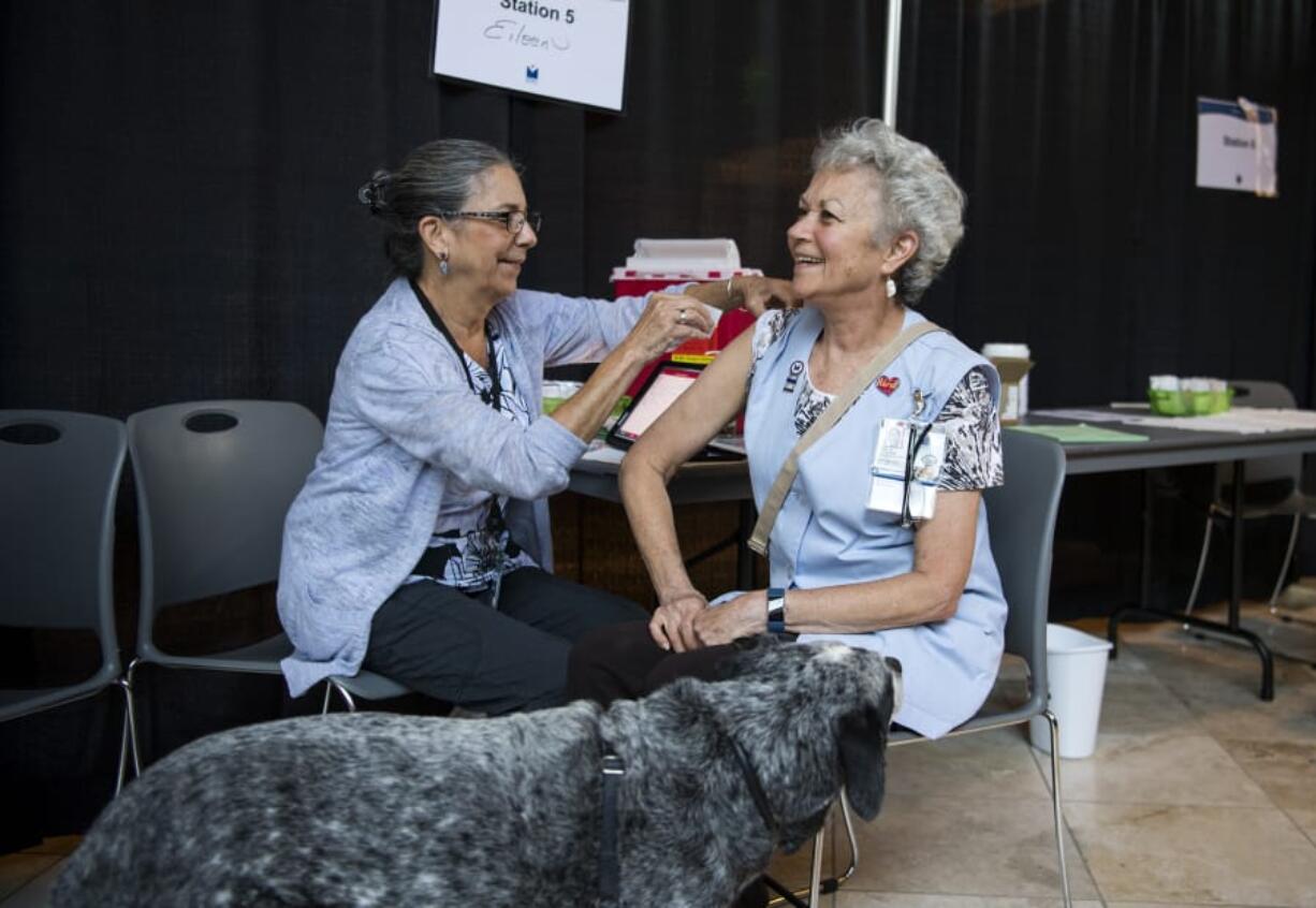 Registered nurse Eileen Langford, left, administers a flu shot to hospital volunteer Gail Greer during the Kick The Flu event for hospital employees at Legacy Salmon Creek Medical Center. Greer and her dog, Truman, are volunteers with the hospital’s Pet Partners animal therapy program.