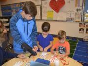 Washougal: Jemtegaard Middle School’s Jaden Cooms, from left, helps Columbia River Gorge Elementary School first-graders Ella Paulson and Tucker Morgan on a project to learn how the human hand works.