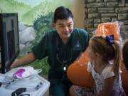 Dr. Ron Hsu looks over X-rays with patient Taryn Hatfield of Washougal, 6, center, and Taryn’s mom Leah, at his practice Storybook Dental in Camas in September.