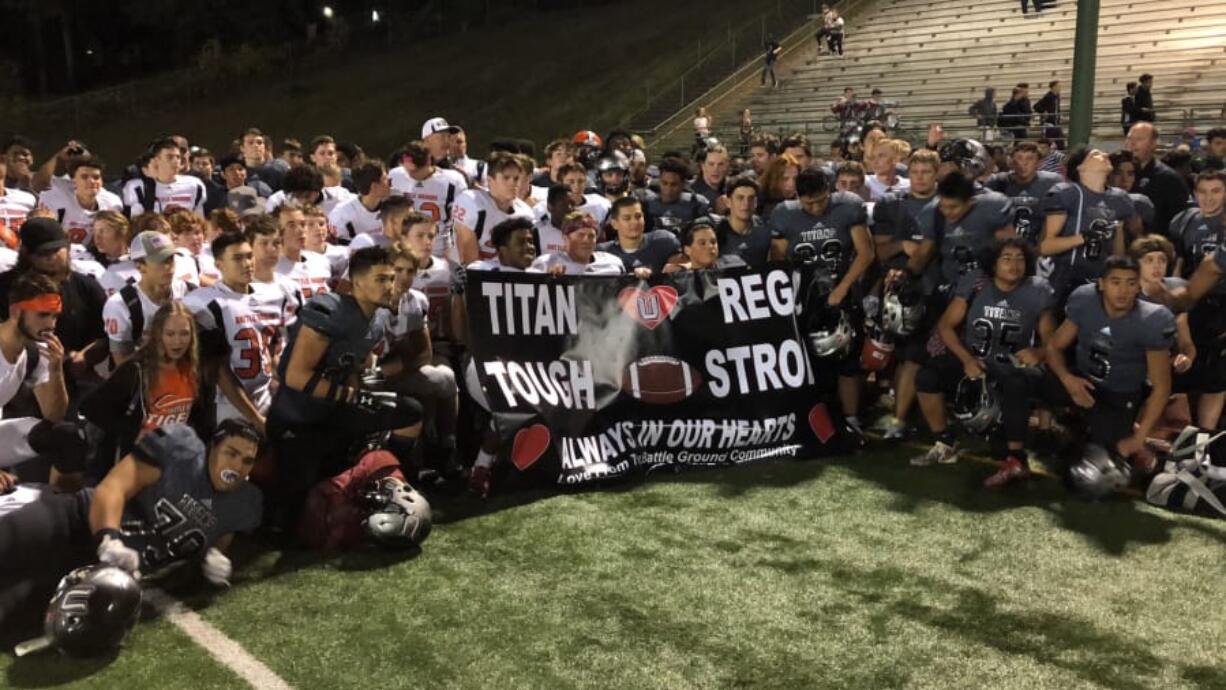 Football players from Battle Ground, left, and Union pose with a banner presented by Battle Ground on Friday at McKenzie Stadium to honor late Union assistant coach Mark Rego, who died Oct. 6 after battling cancer.