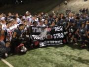 Football players from Battle Ground, left, and Union pose with a banner presented by Battle Ground on Friday at McKenzie Stadium to honor late Union assistant coach Mark Rego, who died Oct. 6 after battling cancer.