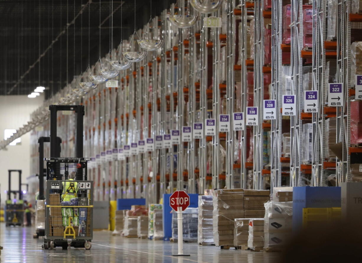 FILE- In this May 3, 2018, file photo an associate guides a vehicle past rows of goods during a tour of the Amazon fulfillment center in Aurora, Colo. Amazon’Äôs announced Tuesday, Oct. 2, that it would raise its hourly minimum wage to $15. Those who already made $15 will get an extra dollar an hour when the change is made next month, but they will also lose two benefits they relied on: monthly bonuses that could top hundreds of dollars and a chance to own Amazon’Äôs sky-rocketing stock, currently worth nearly $2,000.