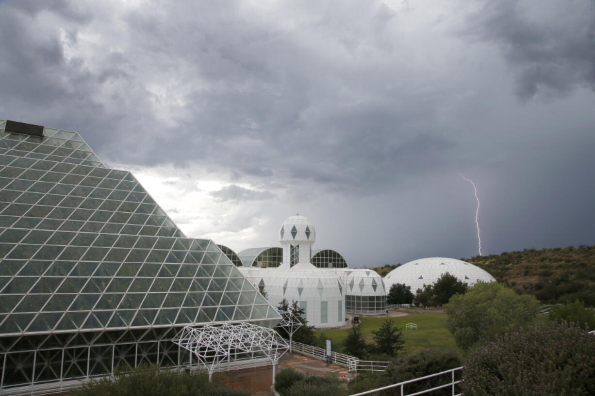 Several of the main buildings of the Biosphere 2 complex, including the tropical rainforest, left, the technosphere, middle, and the south lung, right, are shown as a thunderstorm moves past, in Oracle, Ariz. University of Arizona officials say that 25 years after that New Age-style experiment in the Arizona desert, the glass-covered greenhouse thrives as a singular site for researchers from around the world studying everything from the effects of the ocean’s acidification on coral to ways of ensuring food security. (AP Photo/Ross D.