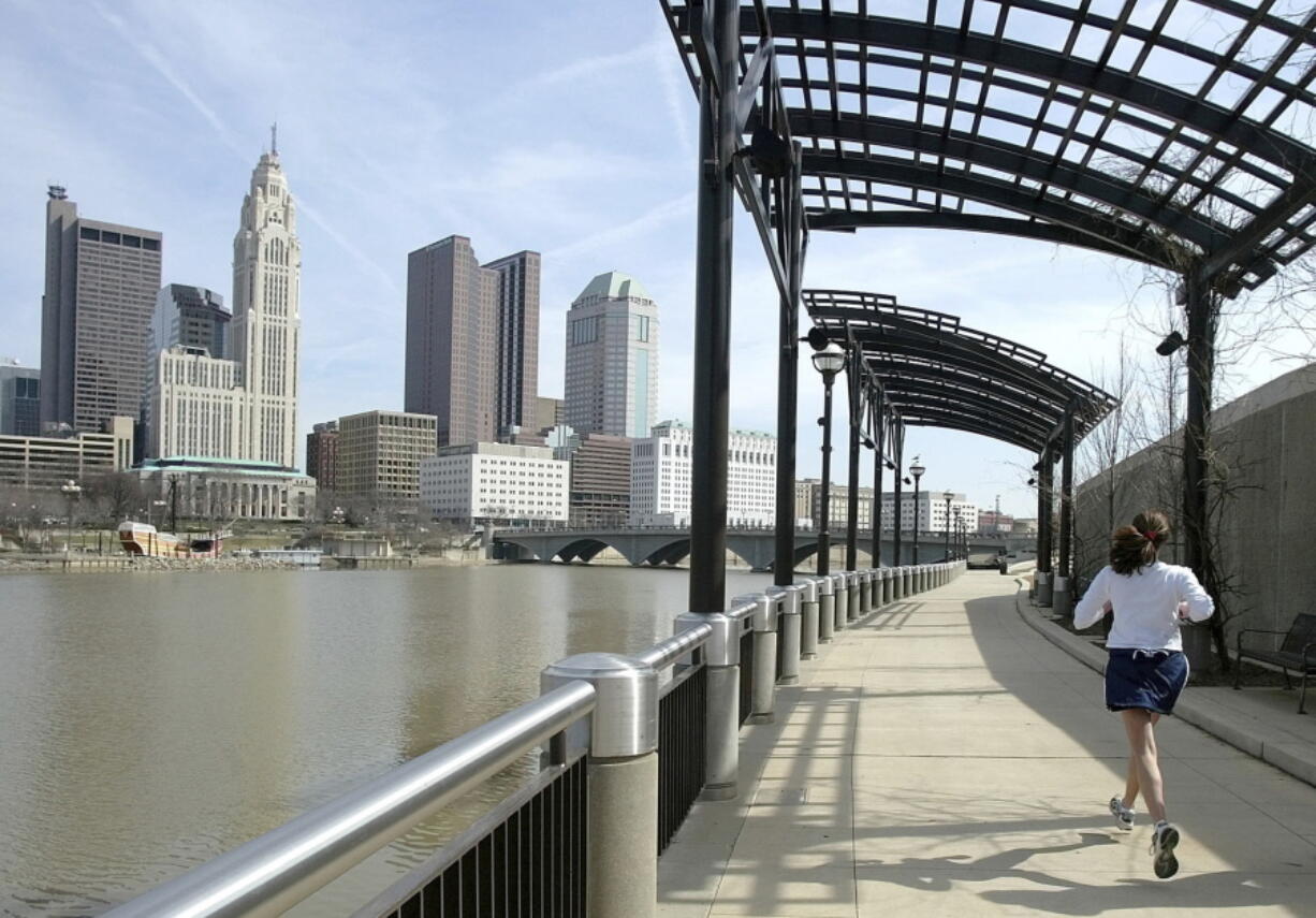 FILE - In this March 15, 2004, file photo, a woman runs the Franklinton floodwall next to the Scioto River in Columbus, Ohio. The largest city named for Christopher Columbus has called off its observance of the holiday named for the explorer. Offices in Columbus, Ohio, will remain open Monday, Oct. 8, 2018, and close on Veterans Day instead.