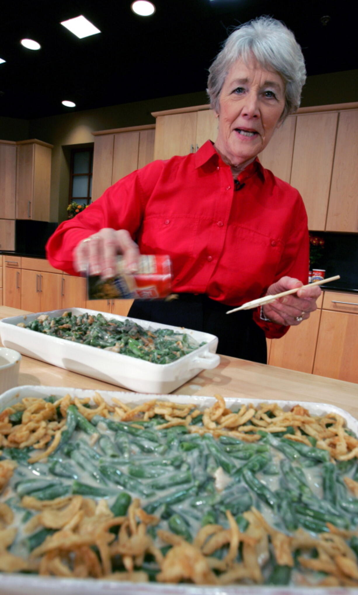 A Green Bean Cassorole sits in the foreground as Dorcas Reilly prepares another at the Campbell Soup Co. corporate kitchen in Camden, N.J. Reilly died on Monday, Oct. 15, 2018 and her family will celebrate her life on Saturday, Oct. 27 in the town where she lived, Haddonfield, N.J. Reilly was a Campbell Soup kitchen supervisor in 1955 when she combined green beans and cream of mushroom soup, topped with crunchy fried onions, for an Associated Press feature. It is the most popular recipe ever to come out of the corporate kitchen at Campbell Soup.