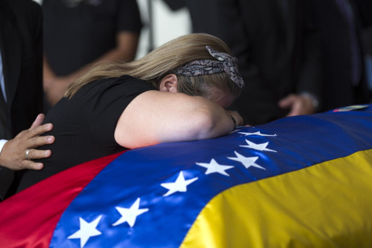 Luz Alban, the sister of opposition activist Fernando Alban, cries over the flag-draped casket containing his remains, during a solemn ceremony at the National Assembly headquarters, in Caracas, Venezuela, on Tuesday. International condemnation of Venezuela’s leadership poured in Tuesday following the suspicious death of the opposition activist authorities say evaded justice by throwing himself from the 10th floor of a police building.