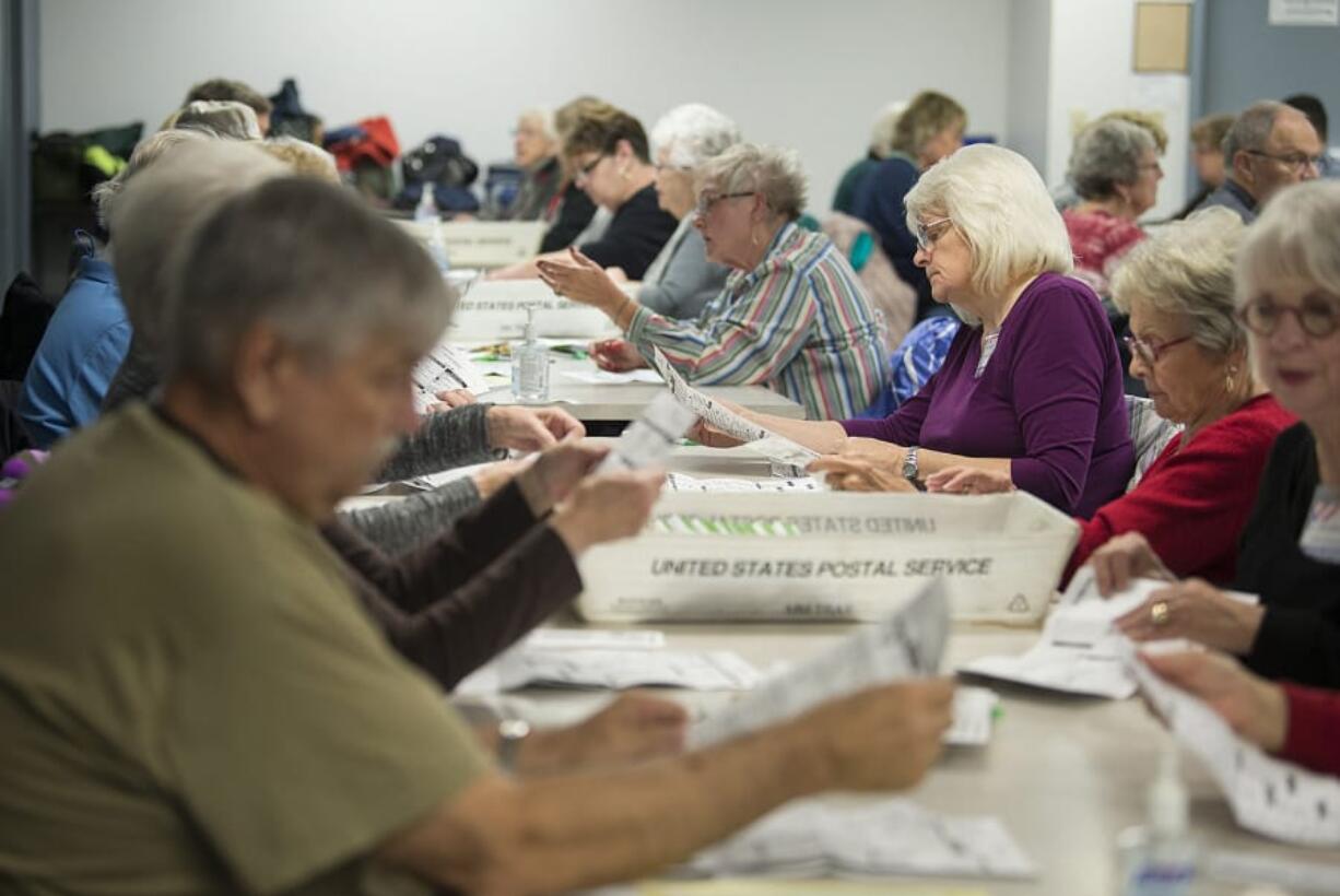 A packed table of election officials including Juanita Berry, wearing purple, sorts through ballots returned so far ahead of the Nov. 6 general election. Auditor Greg Kimsey says a record turnout for a nonpresidential year is possible. At top, stacks of ballots wait to be inspected by officials at the Clark County Elections Office.