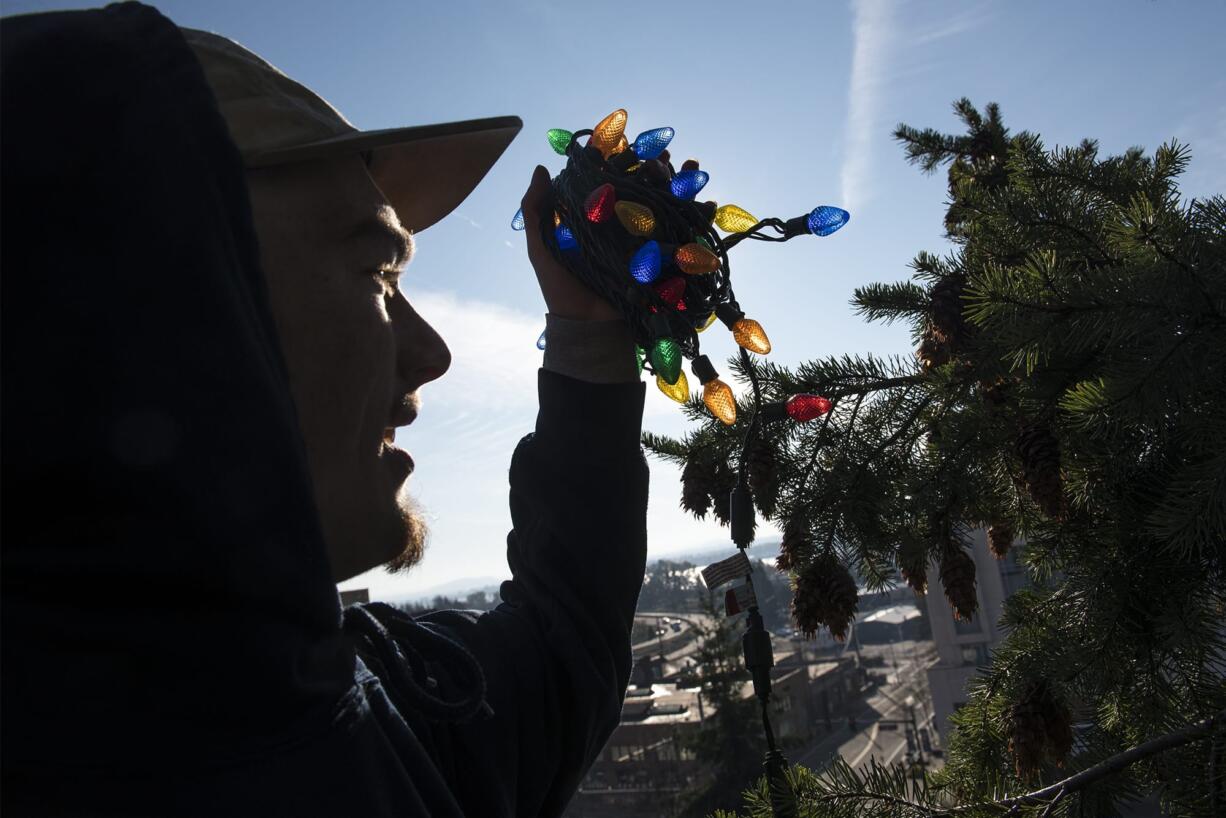 Sam McCostlin with St. Mary’s Services of Vancouver places Christmas lights atop a tree in Ester Short Park on Tuesday morning.