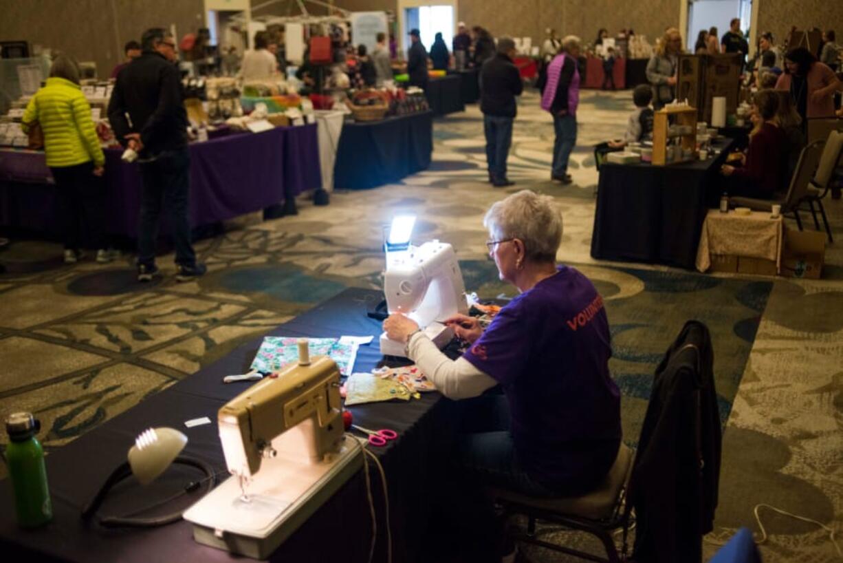 Carol Frana sews reusable gift bags out of recycled fabrics while people shop at the Vancouver Holiday Market at the Hilton Vancouver Washington on Sunday. Volunteers from Repair Clark County, a DIY fix-it group, made the bags, as a means and inspiration to limit personal waste during the holiday season.