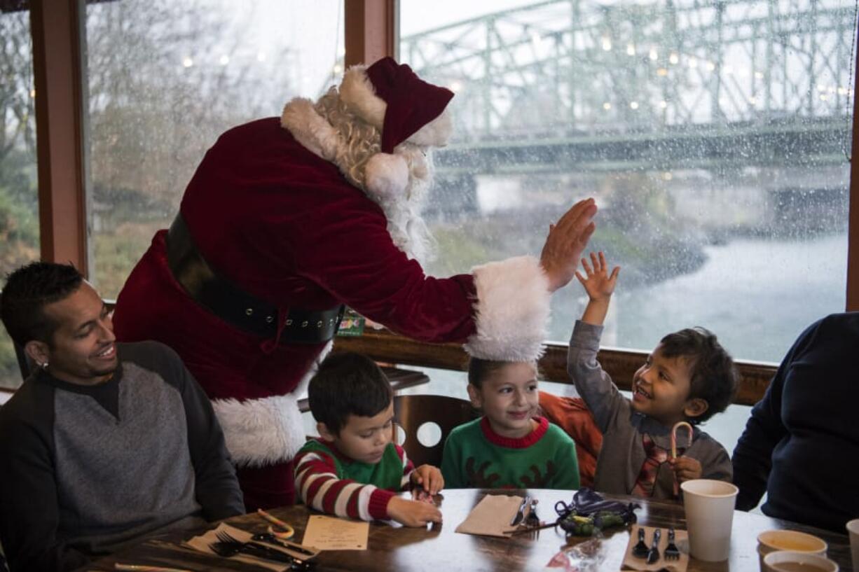 Dressed as Santa, Vince Hochanadel high-fives Rodrigo Solis, 3, both of Vancouver, at the free Thanksgiving meal at WareHouse ’23. Solis’ uncle Victor Gonzalez, from left, and cousins Daniel Reseadiz, 3, and Emily Reseadiz, 6, all of Vancouver, sit beside him. The annual meal is hosted by state Court of Appeals Judge Rich Melnick, Chuck Chronis and Mark Matthias.