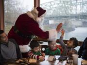 Dressed as Santa, Vince Hochanadel high-fives Rodrigo Solis, 3, both of Vancouver, at the free Thanksgiving meal at WareHouse ’23. Solis’ uncle Victor Gonzalez, from left, and cousins Daniel Reseadiz, 3, and Emily Reseadiz, 6, all of Vancouver, sit beside him. The annual meal is hosted by state Court of Appeals Judge Rich Melnick, Chuck Chronis and Mark Matthias.