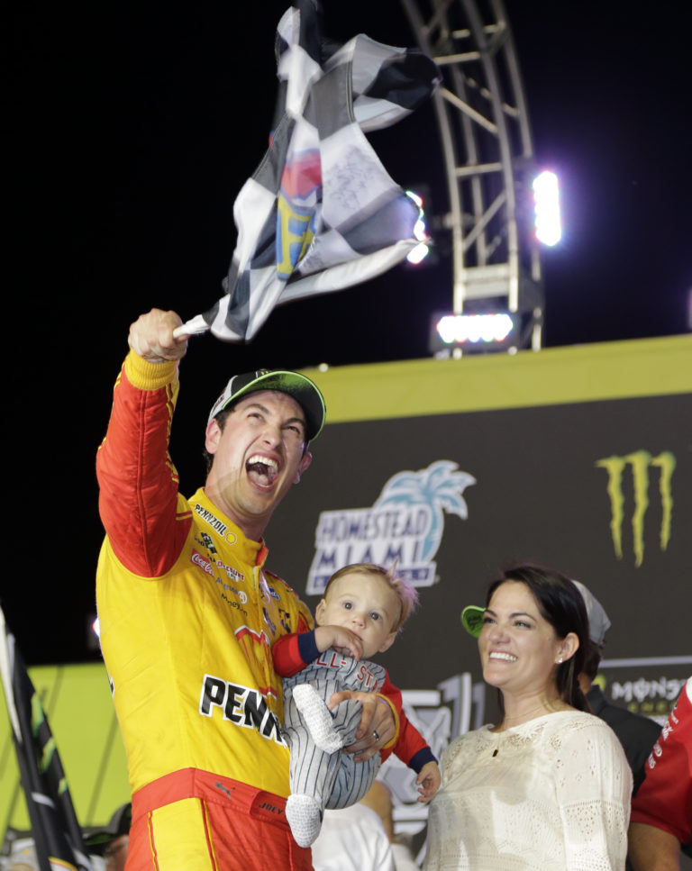 Joey Logano waves a checkered flag as he stands with his wife Brittany Baca and son Hudson after winning NASCAR Cup Series Championship auto race at the Homestead-Miami Speedway, Sunday, Nov. 18, 2018, in Homestead, Fla.