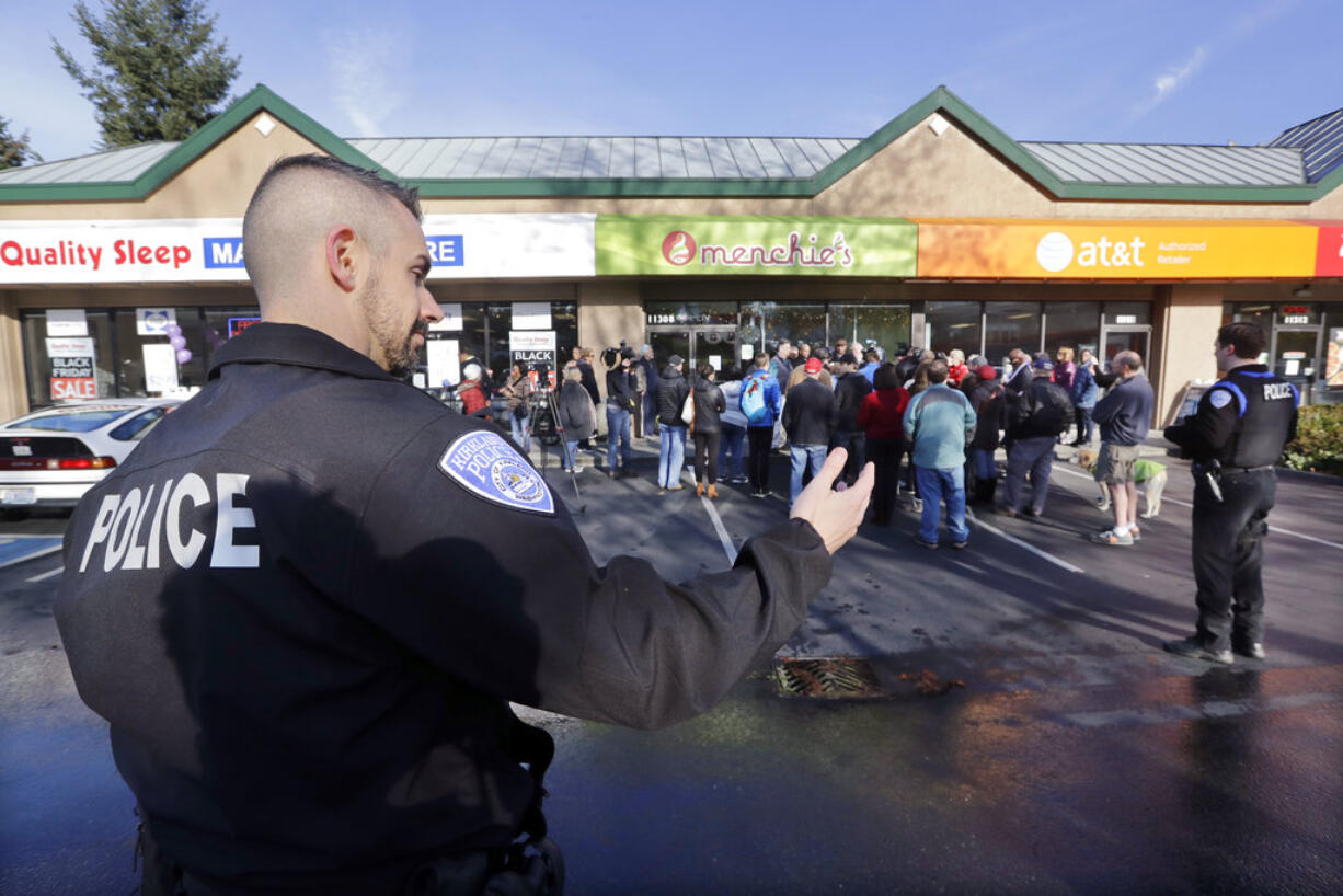 A Kirkland police officer directs traffic past a closed frozen-yogurt shop where Byron Ragland and local civil rights leaders addressed media members Tuesday, Nov. 20, 2018, in Kirkland, Wash. The police department there has apologized for an incident in which officers helped the owner of the Menchie's shop expel Ragland, an African-American man, from the business because employees said they felt uncomfortable. The Seattle Times reported that the shop's owner called police on Nov. 7 about Ragland, who works as a court-appointed special advocate, who was in the shop supervising a court-sanctioned outing between a mother and her son.