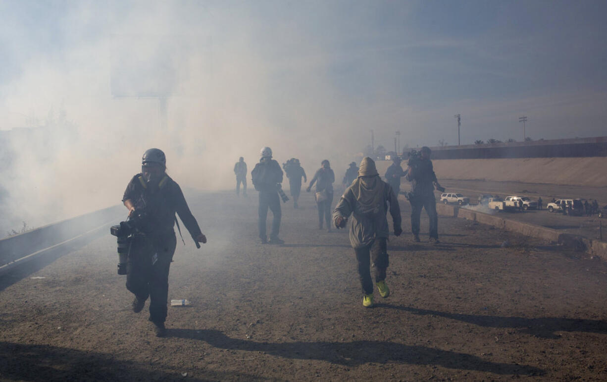 Migrants run from tear gas launched by U.S. agents, amid photojournalists covering the Mexico-U.S. border, after a group of migrants got past Mexican police at the Chaparral crossing in Tijuana, Mexico, Sunday, Nov. 25, 2018. The mayor of Tijuana has declared a humanitarian crisis in his border city and says that he has asked the United Nations for aid to deal with the approximately 5,000 Central American migrants who have arrived in the city.