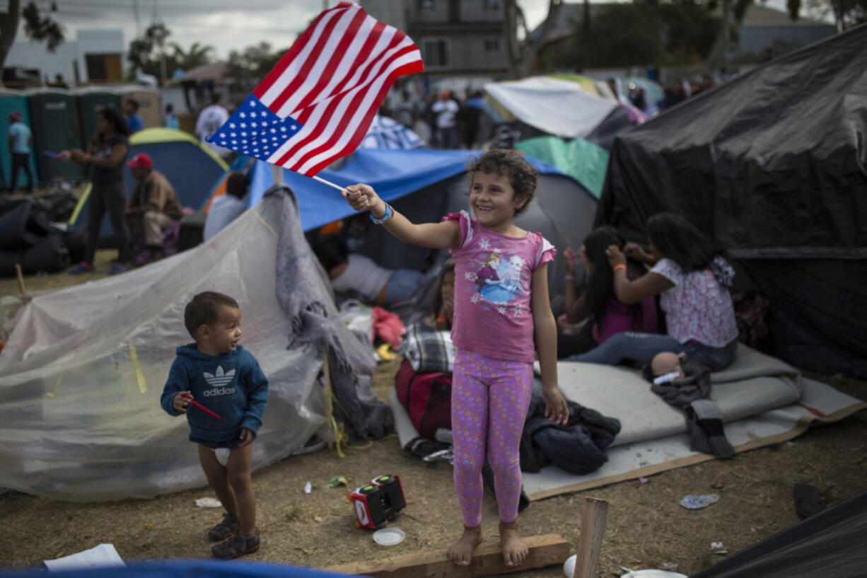 Honduran migrant Genesis Belen Mejia Flores, 7, waves an American flag at U.S. border control helicopters flying overhead Saturday near the Benito Juarez Sports Center in Tijuana, Mexico, which is serving as a shelter for migrants.