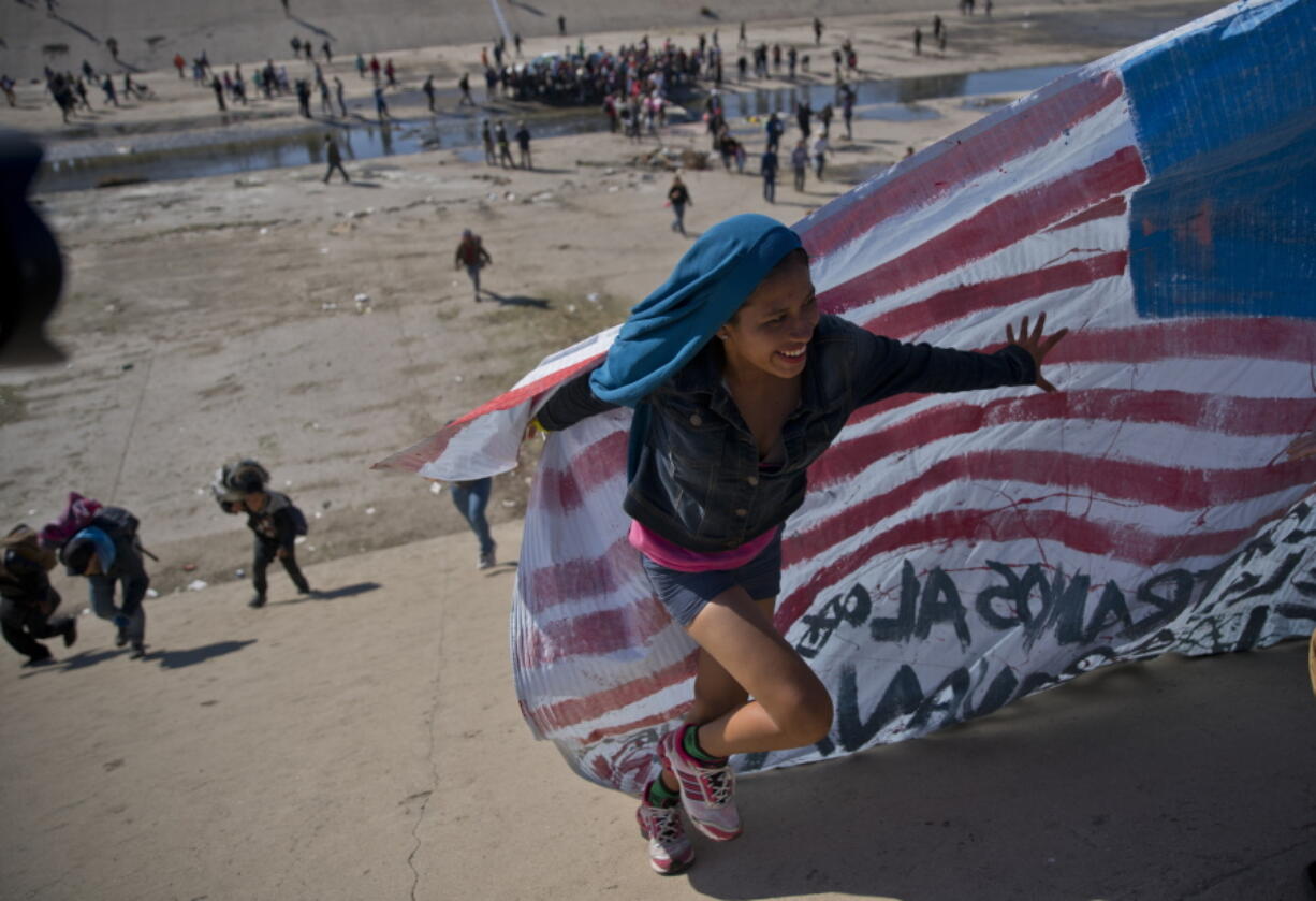 A migrant woman helps carry a handmade U.S. flag up the riverbank at the Mexico-U.S. border after getting past Mexican police at the Chaparral border crossing in Tijuana, Mexico, on Sunday as a group of migrants tries to reach the U.S. The mayor of Tijuana has declared a humanitarian crisis in his border city and says that he has asked the United Nations for aid to deal with the approximately 5,000 Central American migrants who have arrived in the city.