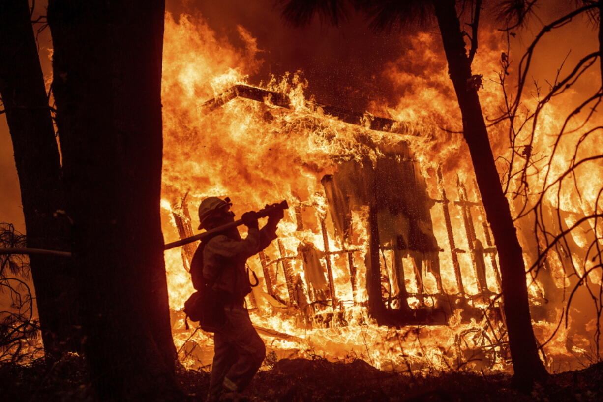 FILE - In this Nov. 9, 2018 file photo, firefighter Jose Corona sprays water as flames from the Camp Fire consume a home in Magalia, Calif. A massive new federal report warns that extreme weather disasters, like California’s wildfires and 2018’s hurricanes, are worsening in the United States. The White House report quietly issued Friday, Nov. 23 also frequently contradicts President Donald Trump.