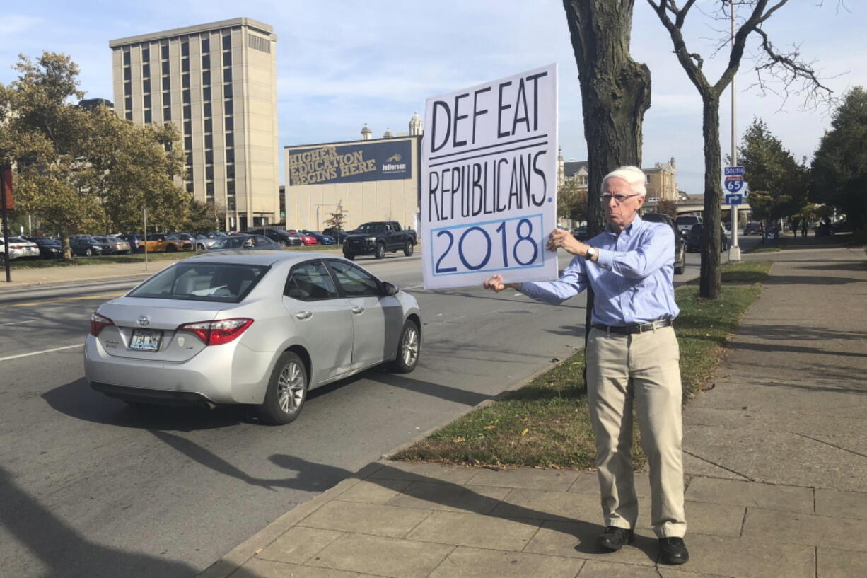 In this Oct. 30, 2018 photo, Michael Gregoire holds a hand-painted sign which reads, “Defeat Republicans 2018,” along a street in Louisville, Ky. “The survival of the country is going to depend on this election,” he said.