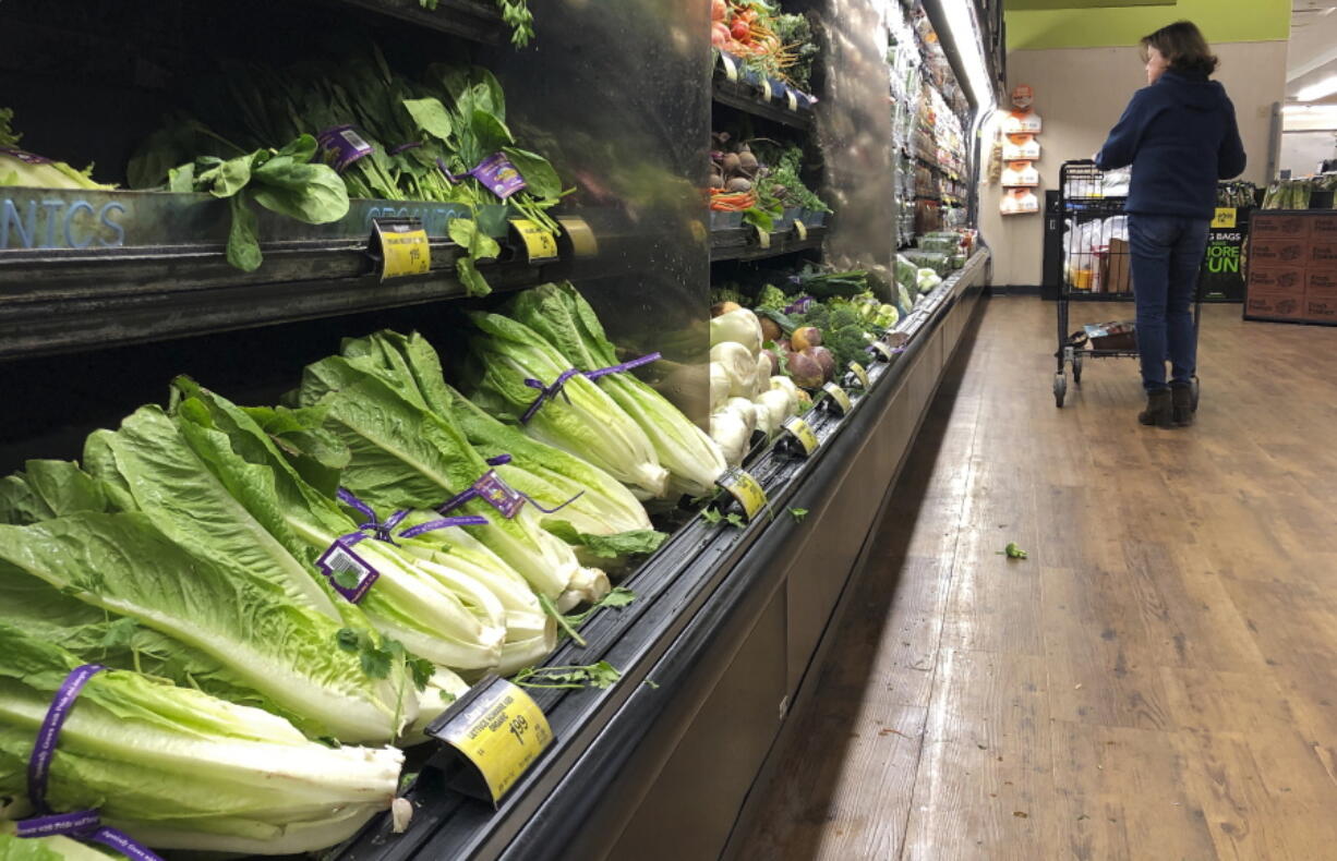 FILE - In this Nov. 20, 2018 file photo, romaine lettuce sits on the shelves as a shopper walks through the produce area of an Albertsons market in Simi Valley, Calif. After repeated food poisoning outbreaks linked to romaine lettuce, the produce industry is confronting the failure of its own safety measures in preventing contaminations. The latest outbreak underscores the challenge of eliminating risk for vegetables grown in open fields and eaten raw. It also highlights the role of nearby cattle operations and the delay of stricter federal food safety regulations. (AP Photo/Mark J.