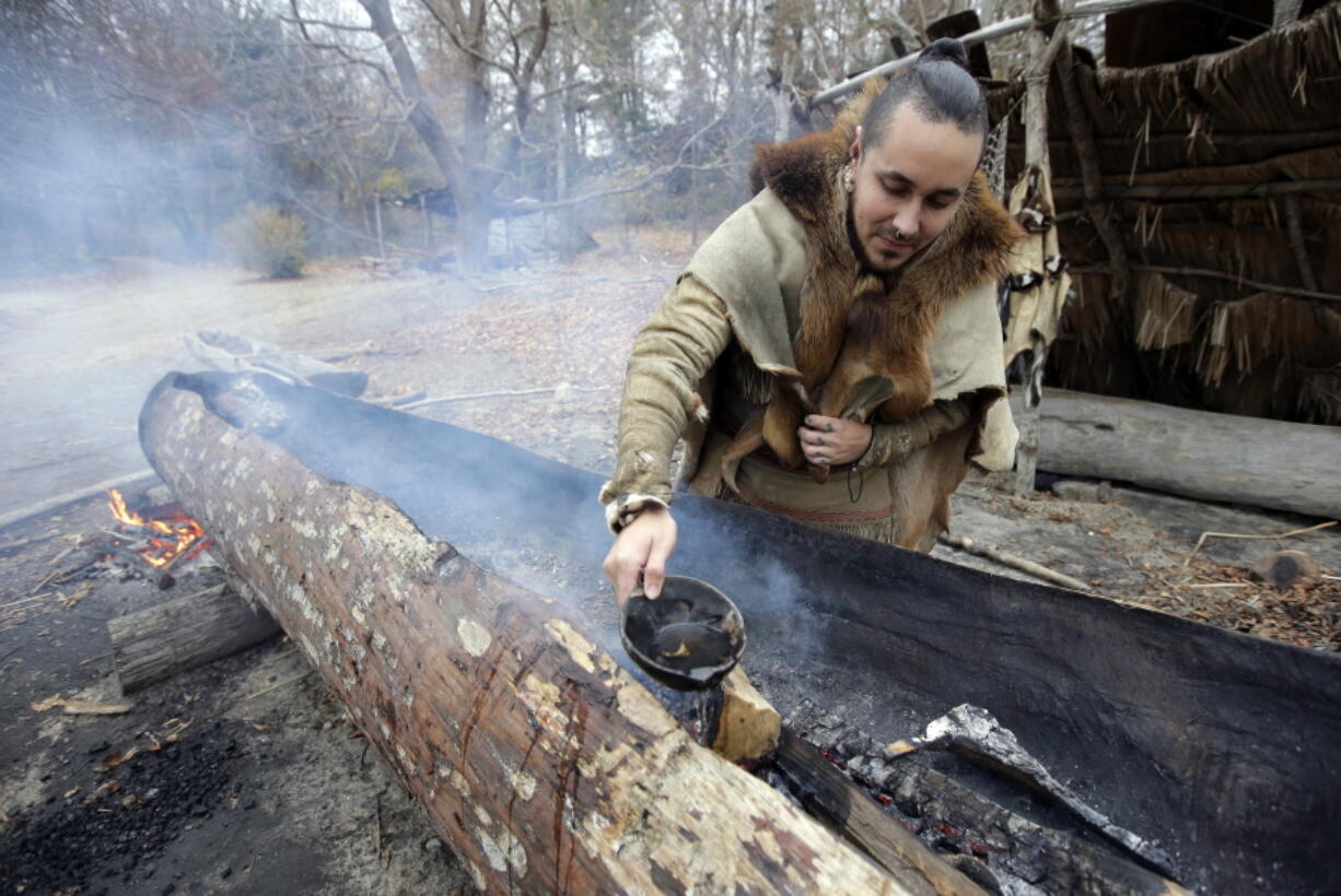 In this Thursday, Nov. 15, 2018, photo, Mashpee Wampanoag Phillip Wynne, of Sagamore, Mass., pours water to control fire and temperatures while making a mishoon, a type of boat, from a tree at the Wampanoag Homesite at Plimoth Plantation, in Plymouth, Mass. Plymouth, where the Pilgrims came ashore in 1620, is gearing up for a 400th birthday, and everyone’s invited, especially the native people whose ancestors wound up losing their land and their lives.