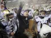 Washington coach Chris Petersen, center, holds the Apple Cup trophy as he celebrates with quarterback Jake Browning, left, and the rest of the team after Washington defeated Washington State 28-15 in an NCAA college football game Friday, Nov. 23, 2018, in Pullman, Wash. (AP Photo/Ted S.