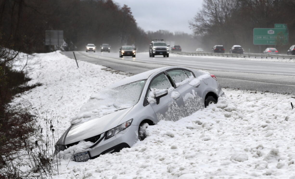 This Thursday, Nov. 15, 2018 photos shows traffic passing by as a car that went off Interstate 684, at the Goldens Bridge exit, during a snowstorm. The first snowfall of the season lingered Friday in the Northeast as thousands of exhausted commuters pointed their fingers at politicians and meteorologists for leaving them creeping along highways or stuck in mass transit hubs.