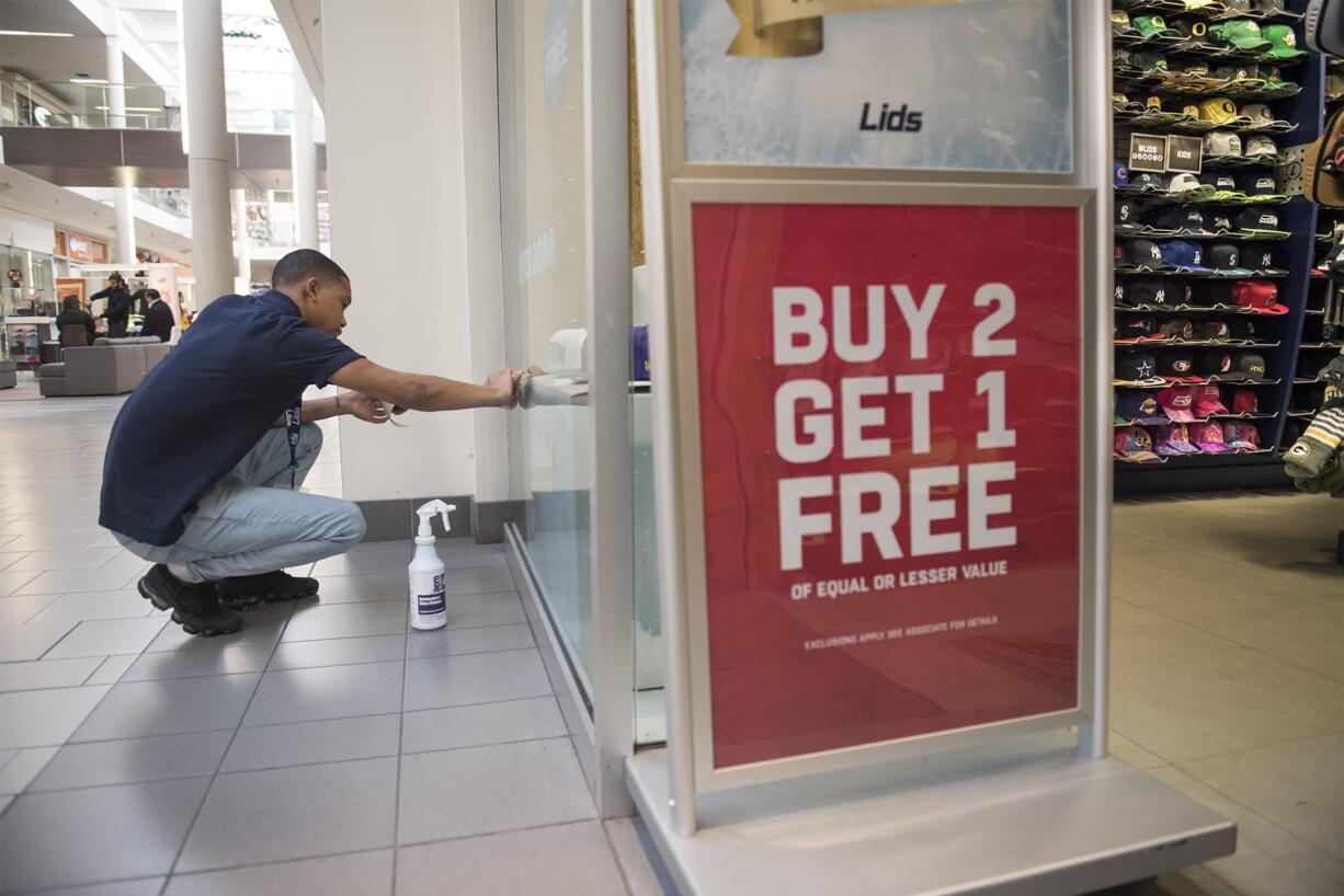 Lids Sales Associate Tavi Pikmey cleans the window of Lids at the Vancouver Mall on Nov. 19. Retail saw big jobs gains in Clark County in November.