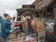 Volunteers Heidi Kartchner, left, and Noah Sarkissian help unload a car filled with Walk & Knock food donations in the parking lot at Chuck’s Produce in Salmon Creek in December 2018.