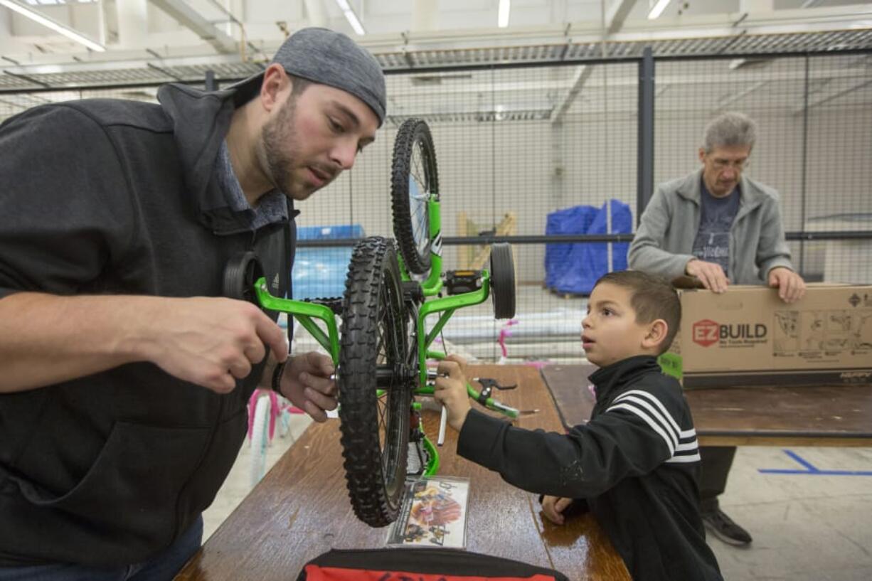 Rylan Ward, 7, and his stepfather Justin Gilson assemble a bike as part of the Scott Campbell Christmas Promise event in Vancouver Saturday. The bicycles will be distributed to needy kids around Clark County.