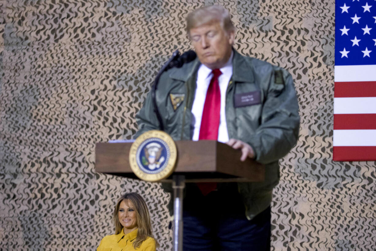 First lady Melania Trump, left, is seated on stage as President Donald Trump pauses as he speaks at a hanger rally at Al Asad Air Base, Iraq, Wednesday, Dec. 26, 2018. In a surprise trip to Iraq, President Donald Trump on Wednesday defended his decision to withdraw U.S. forces from Syria where they have been helping battle Islamic State militants.