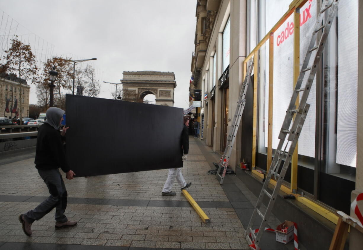 Workers carry a piece of wood as they construct a protective barrier on shop windows Friday along the Champs-Elysees in Paris. Many shop owners across the French capital are getting ready for more violent protests. The Arc de Triomphe is seen in background.