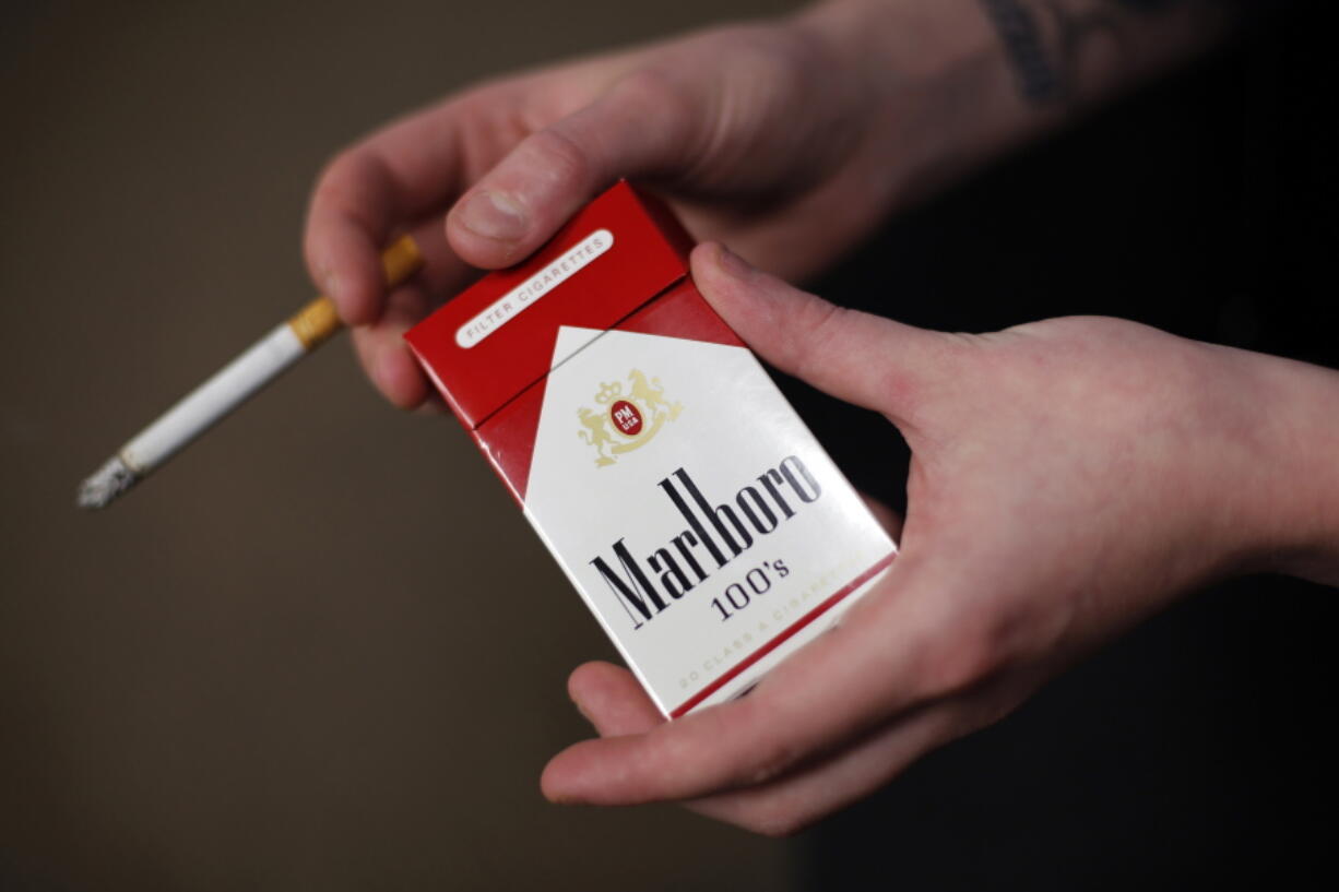 FILE - In this July 17, 2015, file photo, store manager Stephanie Hunt poses for photos with a pack of Marlboro cigarettes, an Altria brand, at a Smoker Friendly shop in Pittsburgh. Altria is diving into the Canadian cannabis market with a $2.4 billion investment in Toronto-based medical and recreational marijuana provider Cronos Group. The investment from Altria Group Inc., would give it about 45 percent ownership of Cronos. Altria will also pay another $1.4 billion for warrants of Cronos Group that if exercised, would give the Altria a 55 percent majority ownership of Cronos. (AP Photo/Gene J.