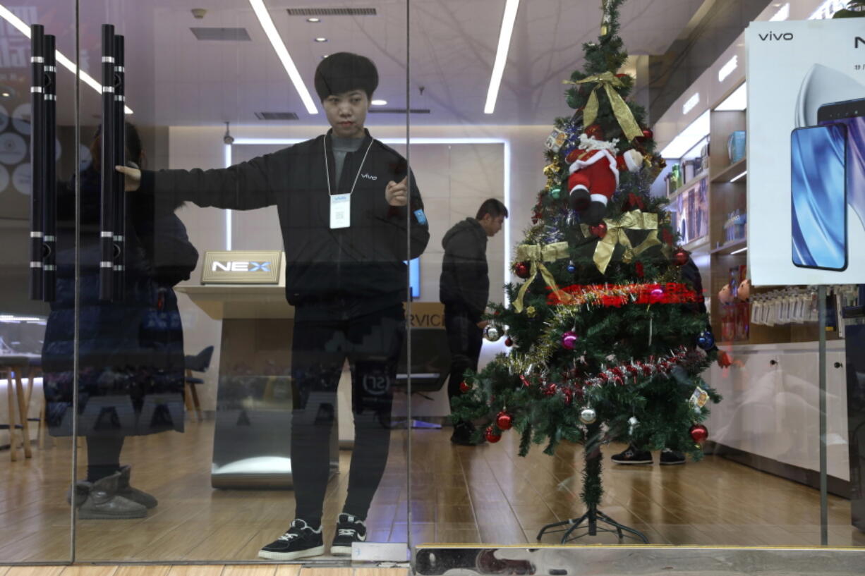 In this Saturday, Dec. 22, 2018, photo, a sales person waits for customers near a Christmas tree decoration in Zhangjiakou in northern China’s Hebei province. At least three Chinese cities have banned Christmas decorations this year. Churches in another city have been warned to keep minors away from Christmas, and at least ten schools nationwide have curtailed Christmas on campus, The Associated Press has found.