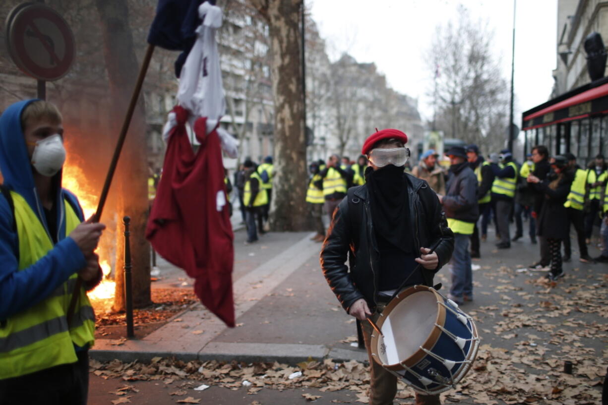 A demonstrator plays a drum Saturday, Dec. 8, 2018 in Paris. Crowds of yellow-vested protesters angry at President Emmanuel Macron and France’s high taxes tried to converge on the presidential palace Saturday, some scuffling with police firing tear gas, amid exceptional security measures aimed at preventing a repeat of last week’s rioting.