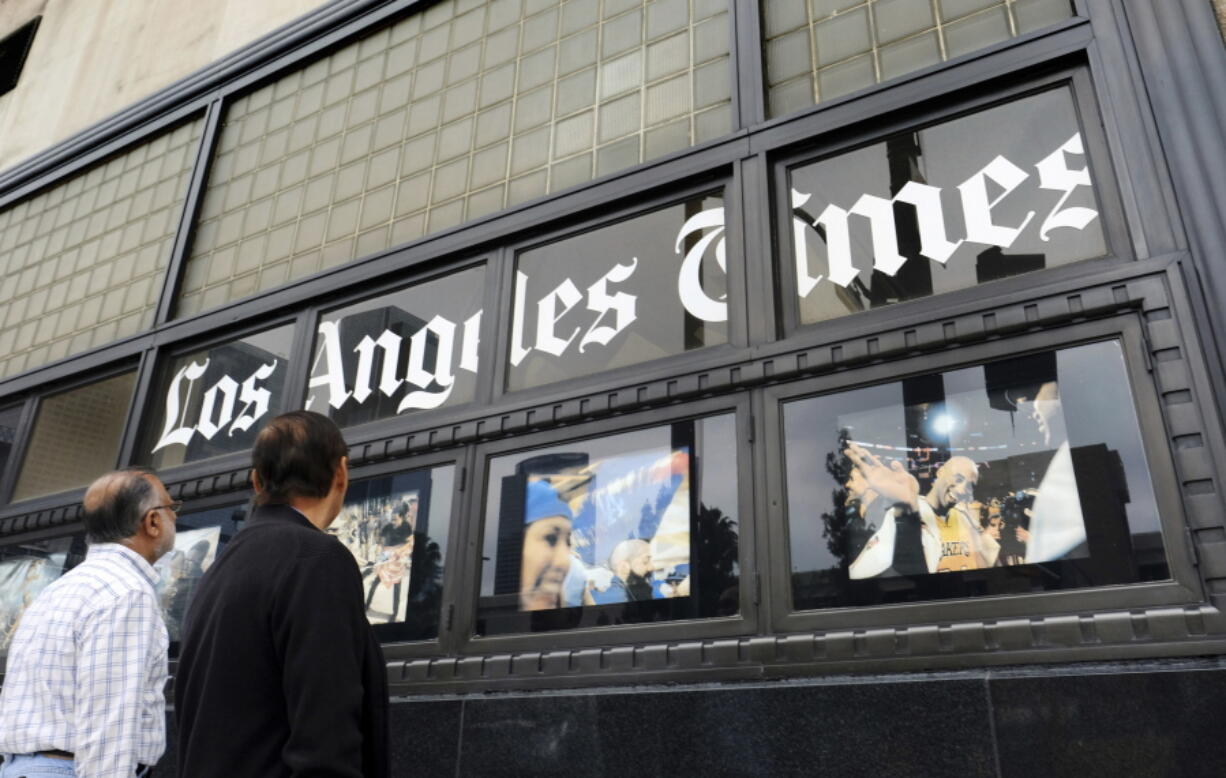 FILE - In this May 16, 2016, file photo, pedestrians look at news photos posted outside the Los Angeles Times building in downtown Los Angeles. A computer virus hit newspaper printing plants in Los Angeles and at Tribune Publishing newspapers across the country. The virus that hit Los Angeles prevented it from printing and delivering Saturday editions of the Los Angeles Times, the San Diego Union-Tribune and other papers to some subscribers.