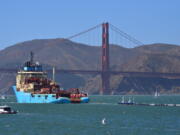 File - In this Sept. 8, 2018 file photo, a ship tows The Ocean Cleanup’s first buoyant trash-collecting device toward the Golden Gate Bridge in San Francisco en route to the Pacific Ocean. The trash collection device deployed to corral plastic litter floating between California and Hawaii in an attempt to clean up the world’s largest garbage patch is not collecting any trash. But Boyan Slat, who launched the Pacific Ocean cleanup project, told The Associated Press in an interview Monday, Dec. 17, 2018, he is confident the 2,000-foot (600-meter) long floating boom will be fixed.