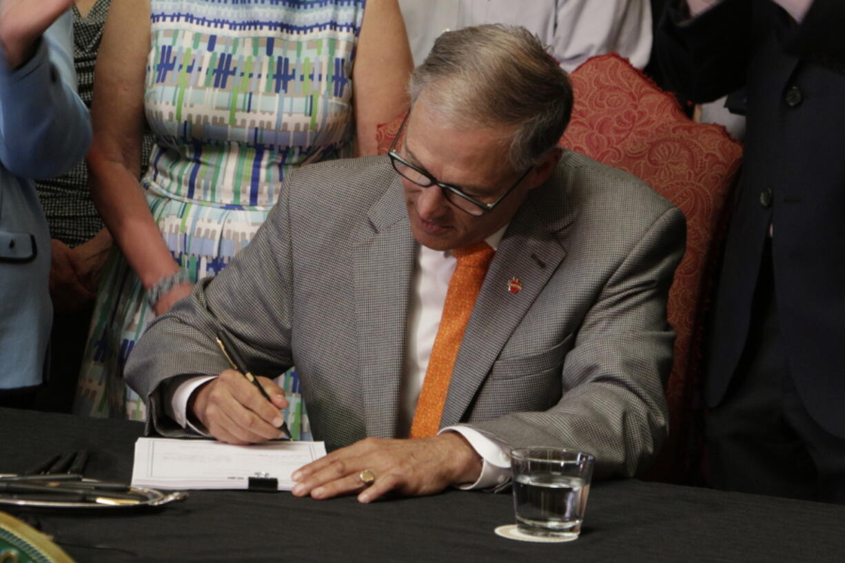 FILE - In this July 5, 2017 file photo, Washington Gov. Jay Inslee signs into law a measure that makes Washington one of a hand full of states that guarantee paid family leave in Olympia, Wash. Employers and employees in Washington state will start paying into a new paid family leave program next week, and benefits from the program will begin in 2020.